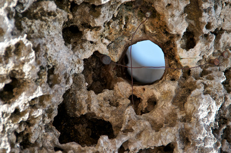 A close up of a large coral rock with a hole and a wire cross through which sky can be seen の写真素材