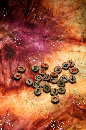 hand carved and painted wooden runes, an ancient alphabet known as the futhark are on a colorful hand dyed fabric with small sparkling beads.の写真素材