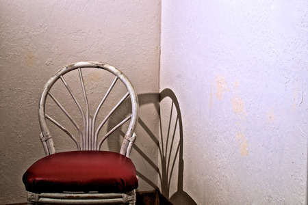 An old white bamboo chair with red vinyl seat in corner of empty room.の写真素材