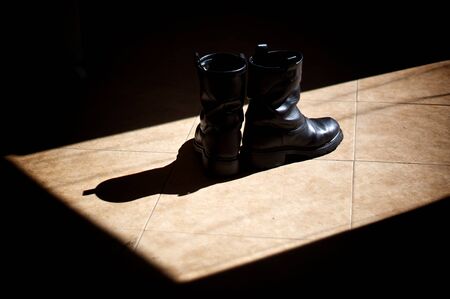 A pair of black leather biker boots standing on a tiled floor in the sunshine, surrounded by shadows.の写真素材