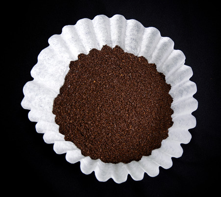 Looking down on a coffee filter with dry grounds on black resembling a flower.の写真素材