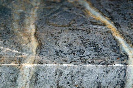 Close up angled view of the edge of a slab of unfinished black soapstone, showing veins and scratches.の写真素材