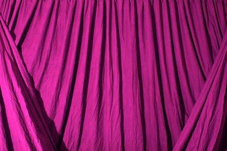 Close up of draped black theatrical curtain or backdrop, lit with pink gel.の写真素材