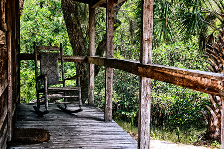 Looking across old wooden porch towards an empty rocking chair with wicker back in tropical estero, florida setting.の写真素材