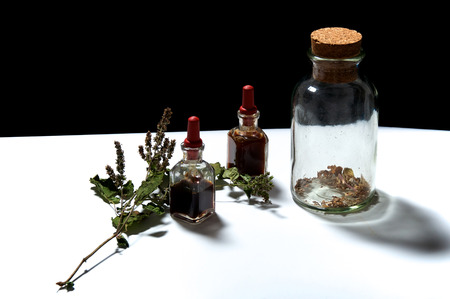 Two small eye dropper bottles with herbal extract essential oils and large jar with dried herbs and patchouli sprig.. Oils are patchouli and rosemary.の写真素材
