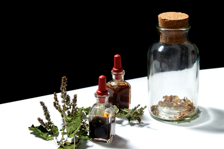 Two small eye dropper bottles with herbal extract essential oils and large jar with dried herbs and dried branch from patchouli plant. Oils are patchouli and rosemary.の写真素材