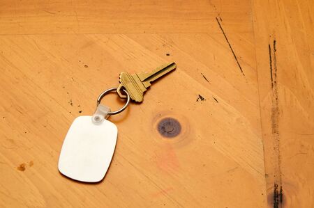 A blank white rubber key fob on keyring with a single brass key laying on old wooden table. Copy space on fob and wood.の写真素材