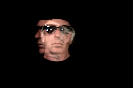 Long exposure image of a man looking in two directions trying to decide which way to go, in sunglasses against a black background.の写真素材