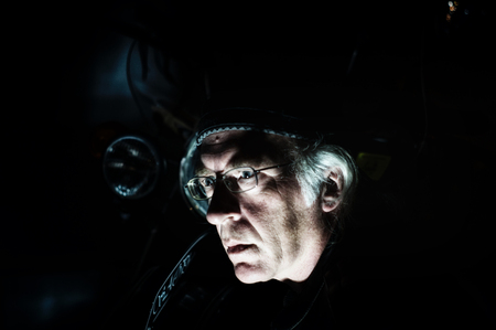 A man with glasses, hat and long white hair. Face is lilt from below and motorcycle can be seen in the shadows.の写真素材