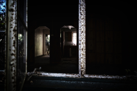 Looking into a dark abandoned home from window showing doorway and kitchen. Noise at 100%