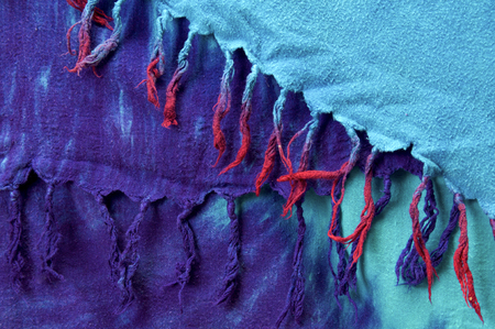Close up of multi colored tie dyed  tassels on fabric background cloth hanging in layers, red, pink and purple on aqua blue.の写真素材