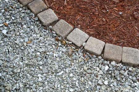 Looking down at square bricks form curve that separates mulch from gravel or small stones in backyard garden area with copy space.の写真素材