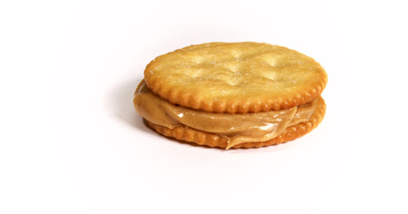 Side view of Natural organic peanut butter filling and oozing out of this sandwich made with golden round crackers on white background.の写真素材