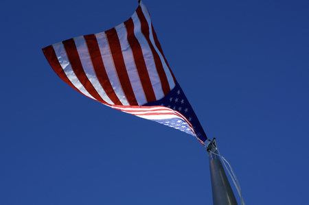 Looking up at American red, white, and blue flag on flagpole from directly below , blowing in the...
