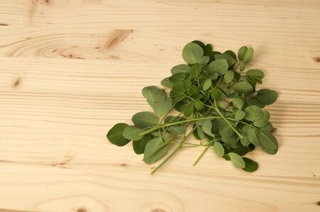 Pile of fresh cut moringa oleifera leaves, also known as drumstick tree on plain wooden background. Known as a superfood and used as alternative medicine.の写真素材