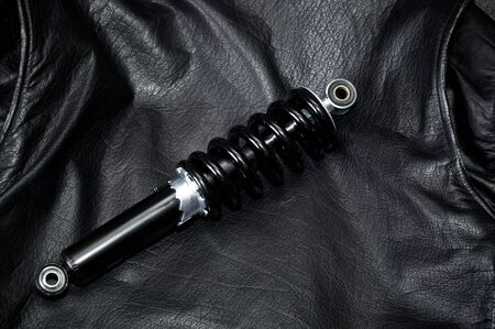 A new clean black and silver motorcycle shock absorber is laying across the back of an old worn leather biker jacket.の写真素材