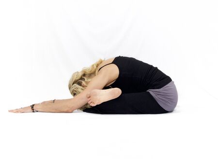 Blonde woman on white background doing seated yoga forward fold pose.の写真素材