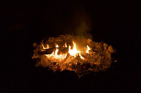 A campfire at night showing logs, flames and burning embers with dark background.の写真素材