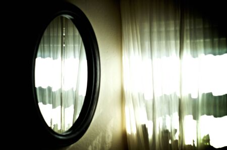 bright sunlight shines through sheer white curtains and is reflected in large oval mirror on wall.の写真素材