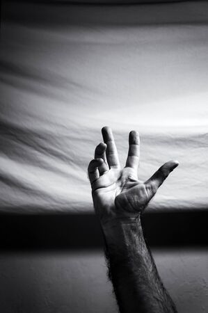 Black and white image of man's arm reaching into the image with right hand palm open.の写真素材