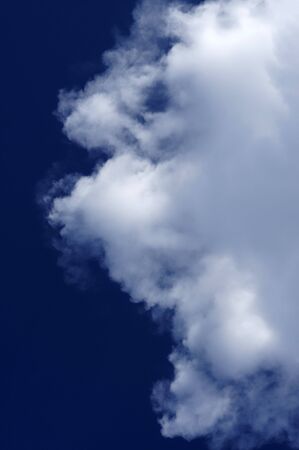 a royal blue sky in vertical format with thick white clouds moving in from right.の写真素材