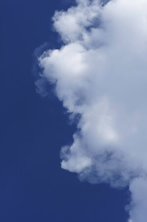 a royal blue sky in vertical format with thick white clouds moving in from right.の写真素材