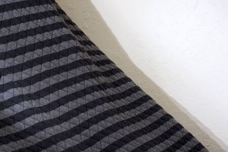 A quilted black and gray striped blanket agains stucco wall at angle.の写真素材
