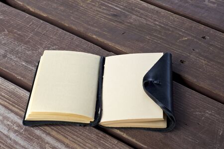 An open leather bound black journal outdoors on table, revealing blank pages, with room for copy.