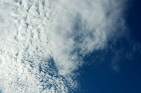 Looking up at a deep blue sky full of various types of clouds, fluffy and wispy.の写真素材