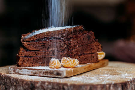 chocolate christmas cake on the wooden bord with mandarins sprinkled wit sugar powder