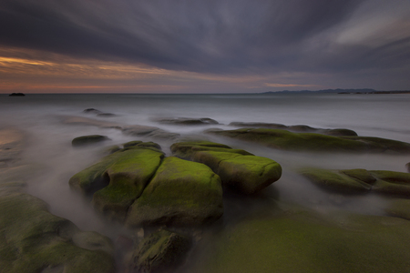 View of sunset at the seaside with a mossy stone in Kudat Sabah Borneo. Long exposure photograph with grain. Image contain certain grain or noise and soft focus.の写真素材