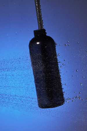 A black bottle of mascara on a blue background with water drops.の写真素材