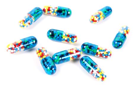 Many identical capsules with varicoloured granules on a white background.