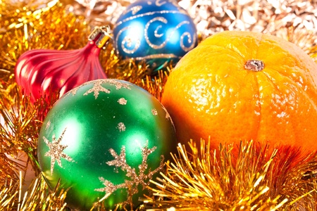 Christmas and new-year decorations. Red beautiful Christmas toy and tangerine on a tinsel backgroundの写真素材