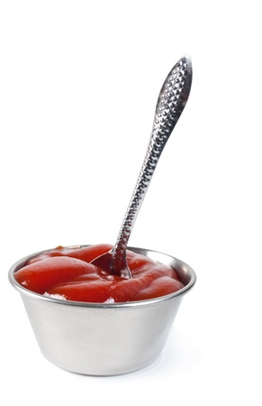 Silver sauce-boat gap-filling a ketchup with a silver spoon on a white backgroundの写真素材