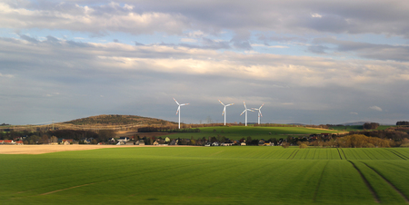 Wind energy business. Wind turbine closeup with blue sky, green grass and villageの写真素材