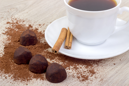 cup of coffee, saucer, truffle chocolates, cinnamon sticks, on wooden backgroundの写真素材