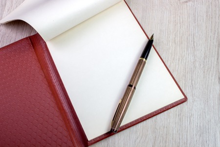 An Open Notebook With White Pages And Gold Fountain Pen On Wood Table. Overhead View