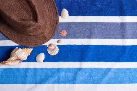 A summer holiday composition on a beach towel with seashells and a hat.の写真素材