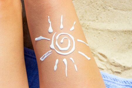Woman sunbathing on the beach with a drawing of sun on her leg with sunscreen cream