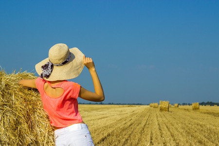 The girl is standing near a straw bale and looking into the distance in the fieldの写真素材