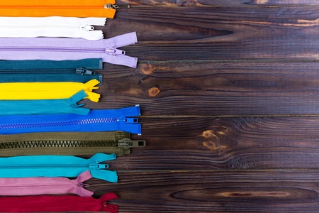 Multicolored zippers are laid out on a wooden tableの写真素材