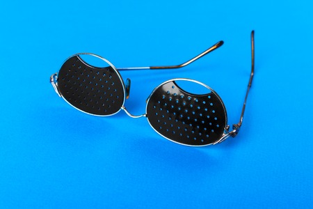 Two different type of glasses on blue background. Medical concept. Top view. Pinhole black eyeglasses help relaxing weary eyes Isolated on white background. Classic Fashion optical eyeglasses.の写真素材