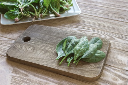cutting board on a table with spinach leaves, a plate of spinach in the background. Meal preparation...