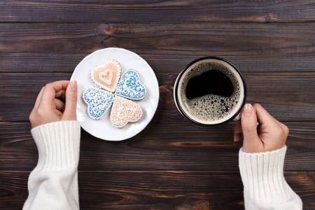 Female hands with coffee and heart shaped cookies on wooden table, top view.の写真素材