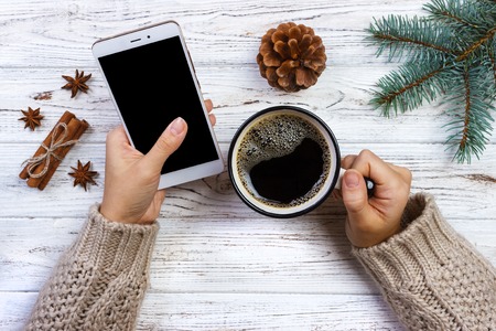 Female holding cup coffee and smartphone and christmas decoration on wooden background.
