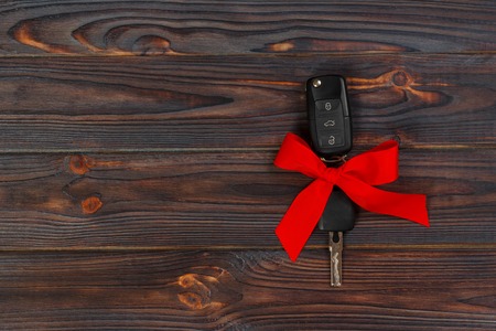 Close-up view of car keys with red bow as present on wooden background.の写真素材