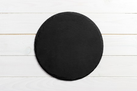 Black slate round stone on wooden background, top view, copy space.