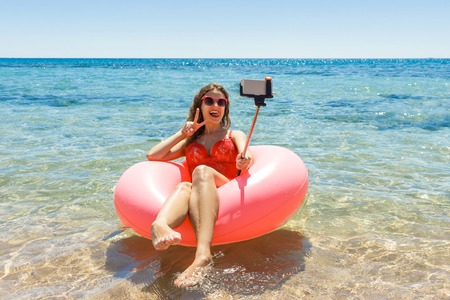Happy Smiling girl makes selfie floating on inflatable donut in sea. vacation time.の写真素材