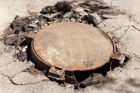 broken metal sewer hatch in the middle of an asphalt road.の写真素材